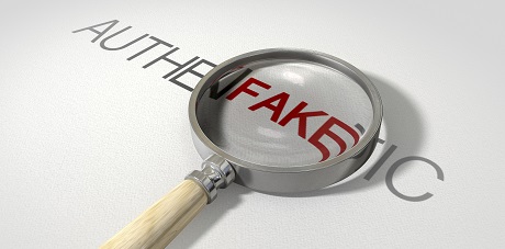 A concept image of a magnifying glass with a wooden handle on a textured white surface showing the word authentic but magnifying the word fake resembling counterfeitting